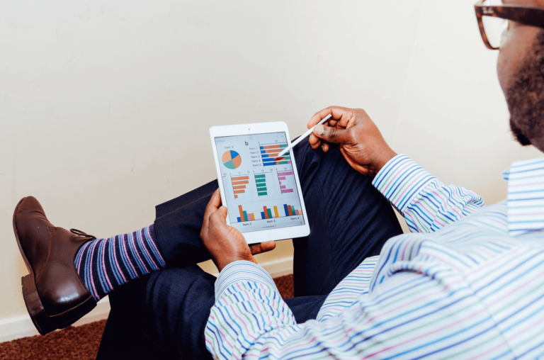 Man met kleurrijke sokken analyseert met een tablet de KPI's op een dashboard.
